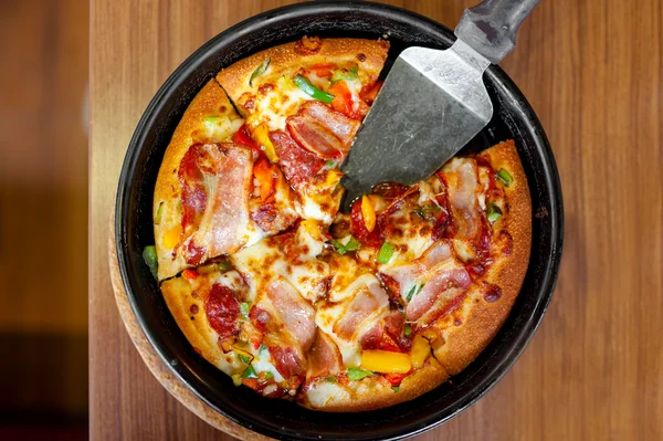 Supreme delicious fresh pizza with bacon, ham and vegetables served on hot iron plate — Stock Photo, Image