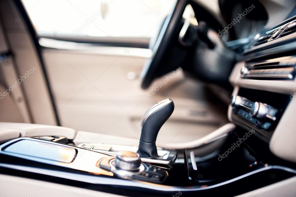 Modern beige interior of new car, close-up details of automatic  transmission and gearstick against steering wheel background and dashboard