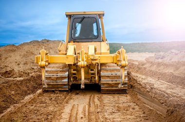 Bulldozer with steel blade moving soil and sand around and working in a sandpit on construction site of a house, road or industrial hall clipart