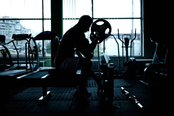 Silueta de un atleta haciendo ejercicio en el gimnasio. Entrenamiento de levantador de pesas en el gimnasio —  Fotos de Stock