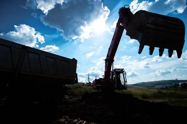 Silhouette of industrial excavator loading earth into a dumper truck at construction site — Stock Photo, Image