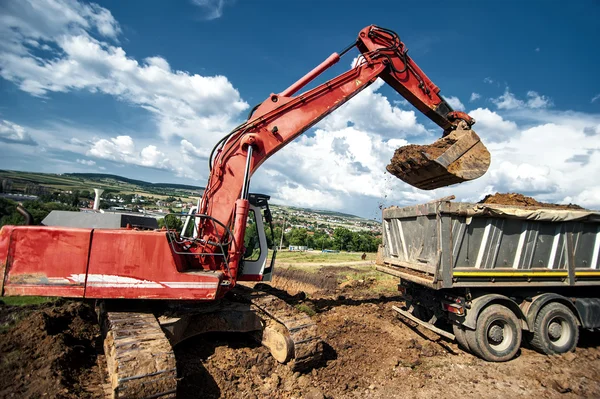 Промисловий екскаватор завантажує ґрунтовий матеріал з дорожньо-будівельного майданчика у вантажівку-носій — стокове фото