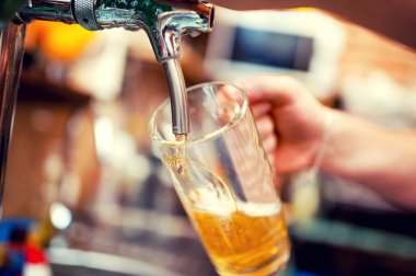 Barmen elini bira fıçısına koyup bira dökerken yakın plan.