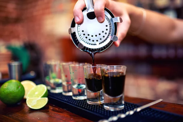 Barman mezclando y vertiendo un cóctel alcohólico de verano en pequeños vasos de chupito en el mostrador —  Fotos de Stock