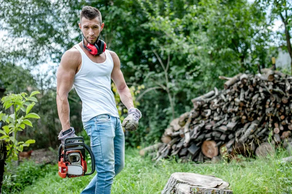 Porträtt av uttrycksfulla muskulös skogshuggare, man med motorsåg och linne i skogen — Stockfoto