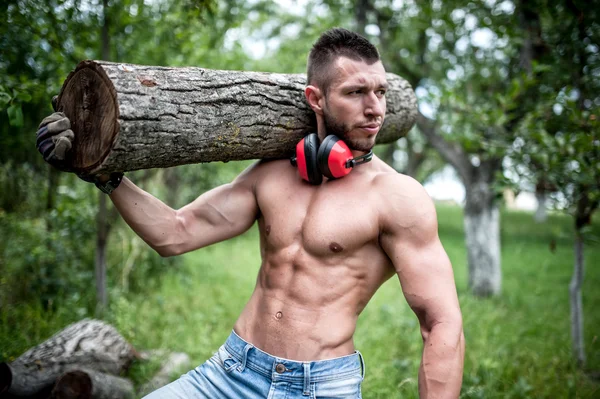 Knappe mannelijke model logs, snijden brandhout en poseren verplaatsen — Stockfoto