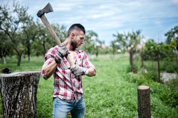 Athletic male lumberjack cutting logs for firewood with axe — Stock Photo, Image