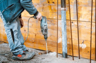 Worker using a drilling power tool on construction site and creating holes in concrete