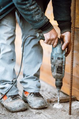 Builder working with rotary hammer drill perforator equipment making holes in concrete on construction site