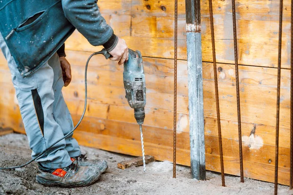 Worker using a drilling power tool on construction site and creating holes in concrete