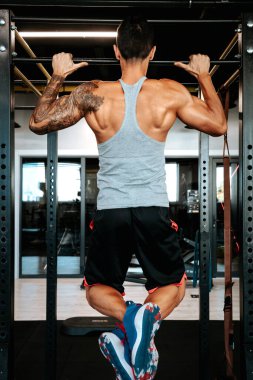 Spor salonunda çalışan profesyonel bir sporcunun portresi, barfiks çekmek ve sırt antrenmanı yapmak.