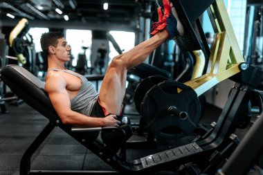 Spor salonunda spor yapan profesyonel bir sporcu, ağırlık çalışırken bacak egzersizi yapıyor. Spor salonunda kaslı bir adam ağırlık kaldırıyor.