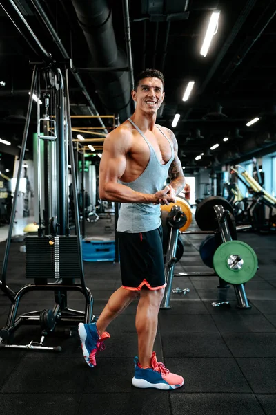 プロの健康トレーナーと認定トレーナーが動作します ジムで働く筋肉の魅力的な男の肖像 足の筋肉のトレーニングと曲げ筋肉を行う — ストック写真