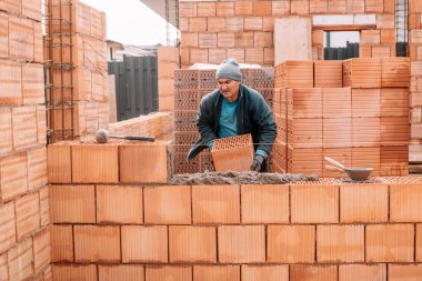 İnşaat alanına tuğla döşeyen endüstriyel erkek duvarcı. İnşaat alanı, duvar inşaatı