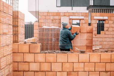 İnşaat alanına tuğla döşeyen endüstriyel erkek duvarcı. İnşaat alanı, duvar inşaatı