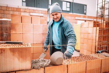 Endüstriyel detaylar - Tuğla, harç ve plastik çekiçle gülümseyen ve duvar inşa eden inşaat işçisi