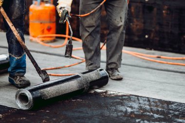 İnşaat işçileri kaynak makinesiyle zarı su geçirmez yalıtım sistemi kuruyorlar.