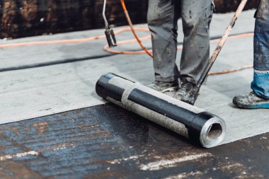 Su geçirmez zarı yapıştırmak için kaynak makinesi ve alev kullanan profesyonel inşaat işçilerinin detayları.