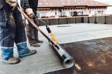 İnşaat işçileri, çatı ustaları yeni evin su geçirmez hale getirilmesi için su geçirmez zar döşüyorlar. Ev su yalıtımı ve yalıtımı