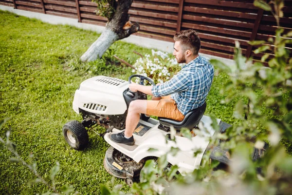 Gardener driving a riding lawn mower in a garden. Professional landscaper using tractor at mowing law