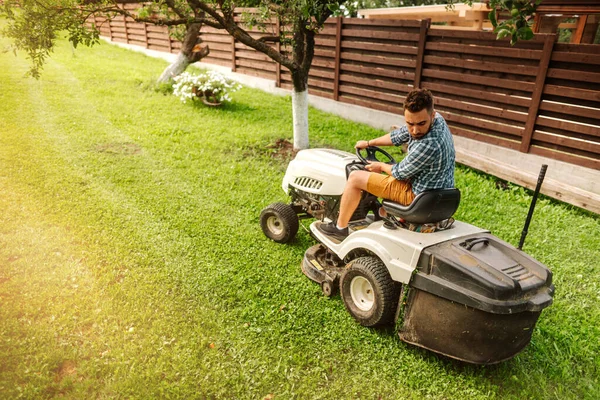 ライドオントラクター 芝生トラクターを使用して産業ハンサムな労働者 トラクターや太陽光線で芝刈りの詳細 — ストック写真