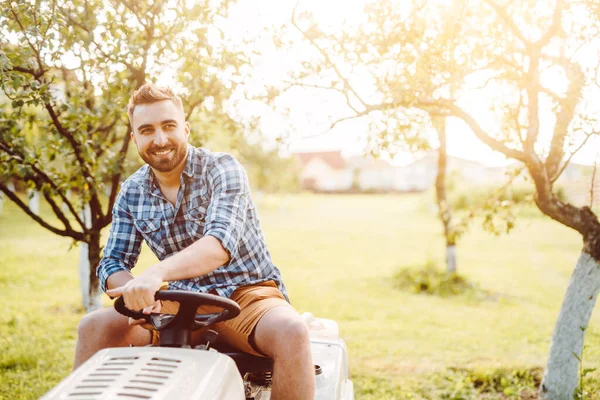 Gardener driving a riding lawn mower in a garden. Professional landscaper using tractor at mowing law