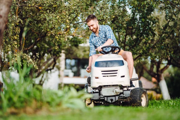 Gardener driving a riding lawn mower in a garden. Professional landscaper using tractor at mowing law