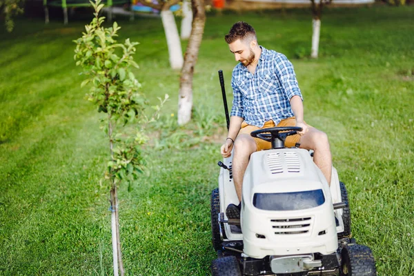 Industrial gardener driving a riding lawn mower in a garden. Professional landscaper using tractor and mowing law