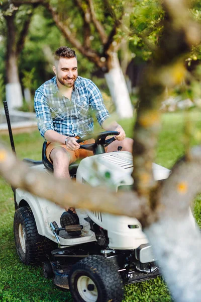 Close up details of landscaping and gardening. Worker riding industrial lawnmower