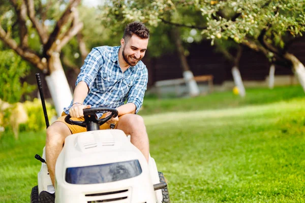 Gardening details with worker using a ride on tractor, mower for cutting grass