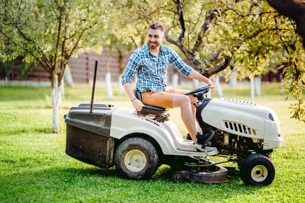 Man using lawn tractor for mowing grass in household garden. Landscaping works with professional tools