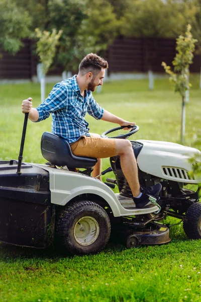 Gardener using lawn tractor for mowing grass in garden. Landscaping works with professional tools