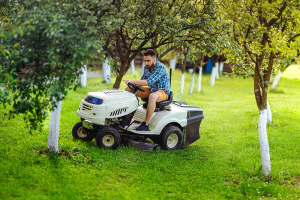 Man using lawn tractor for mowing grass in garden. Landscaping works with professional tools