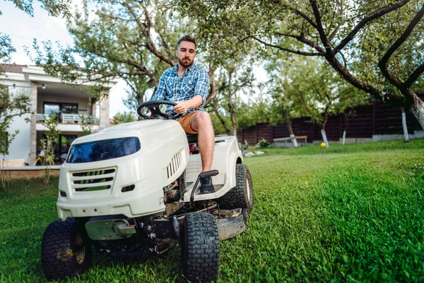 Gardener driving a riding lawn mower in a garden. Professional landscaper using tractor at mowing law