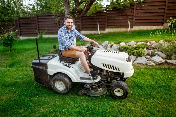 Gardener driving a lawn mower tractor in a garden.