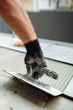 Döşeme ve döşeme. Profesyonel inşaat işçisinin eli balkondaki zemin fayanslarını yapıştırıcı yüzeyine yerleştiriyor.