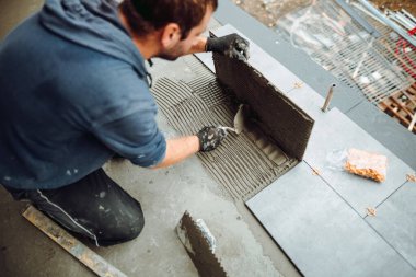 workers hands installing ceramic tiles on the balcony floor. a handyman using a tile spacer to adjust the tile level. Repair work, construction details