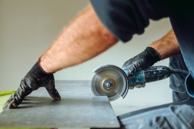 Profesyonel Kafkasyalı inşaat işçisi seramik fayansları döşeme işleri sırasında açı öğütücüyle kesiyor.