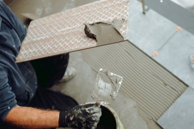 Profesyonel inşaat işçisi, tiler yapıştırıcı döşeyip seramik fayansları balkon zeminine yerleştiriyor. Ev yenileme ve inşaat işlerinin ayrıntıları