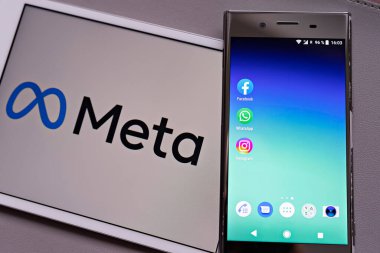 Facebook, WhatsApp ve Instagram uygulamalarının logosu ile beyaz arka plan tablet monitöründeki bulanık META logotype karşısındaki akıllı telefon görüntüsü: Tallinn, Estonya - 29 Ekim 2021