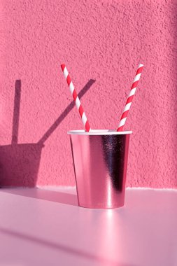 Tek kullanımlık pembe bardakta, duvarda gölgeli saman var. Yakın plan. Noel, pembe noel soyut içecek konsepti