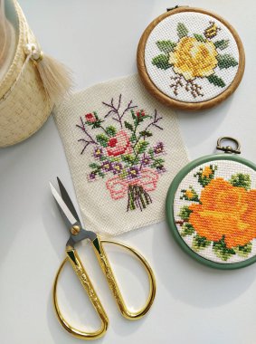Klasik ahşap nakış halkaları, makas, iğne, iplik ve kumaş. Çiçeklerle bembeyaz, düz yere işlenmiş.