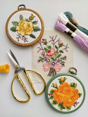 Klasik ahşap nakış halkaları, makas, iğne, iplik ve kumaş. Çiçeklerle bembeyaz, düz yere işlenmiş.