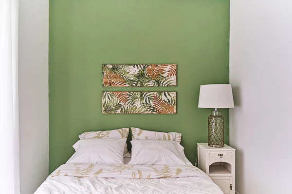Modern bedroom in green and beige tones with tropical print, bed bedside table and table lamp