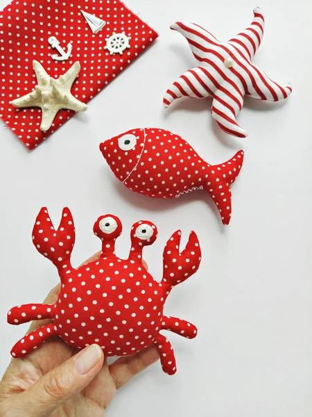 Handmade cartoon stuffed toys in hand, sea life octopus, crab, fish and seahorse. Toy crab, octopus, starfish, seahorse, and fish. DIY Flat lay