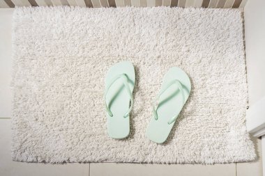 Pair peppermint-coloured flip-flops on white carpet in bathroom. Concept of cleanliness and personal care, top view