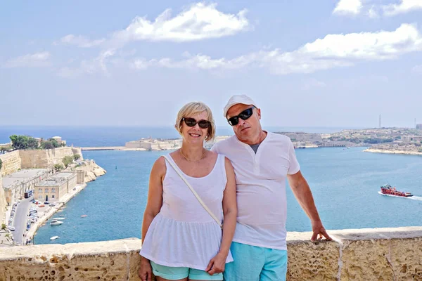 Middle-aged couple of baby boomers people posing for photograph opposite blue sea in Valletta in Malta on sunny summer day. Travel boom after end of coronavirus concept
