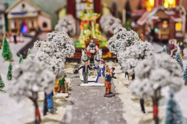Miniature figures of man in tuxedo and lady in dress, coachman and carriage in miniature winter park. Miniature toy city during winter season. City scene in miniature models