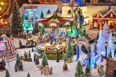 Cheerful miniature carousel with toy people in winter park during Christmas market. Miniature toy city during the winter season. City scene in miniature models