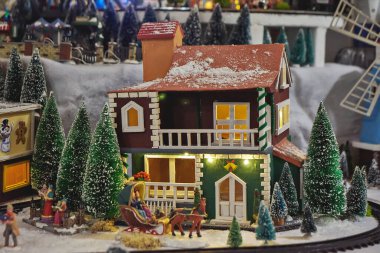 Miniature colored houses and figures of people during celebration of Christmas, snowy streets, and glowing lanterns. Miniature toy city during winter season. City scene in miniature models